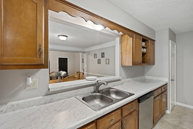 kitchen featuring brown cabinetry, a textured ceiling, stainless steel dishwasher, a sink, and light countertops
