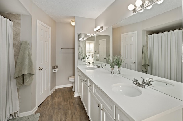 full bath featuring double vanity, wood finished floors, a sink, baseboards, and toilet