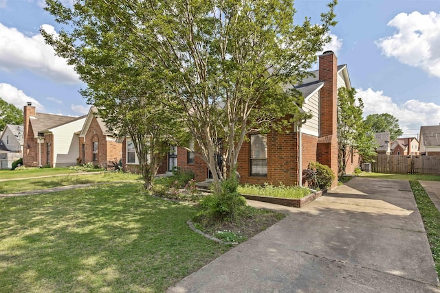 view of property hidden behind natural elements featuring fence, brick siding, a front yard, a chimney, and concrete driveway