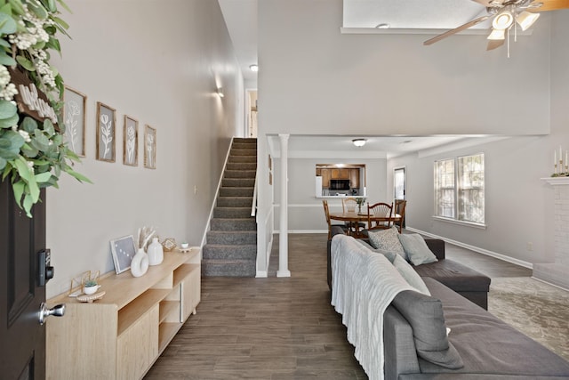 living area with stairway, a high ceiling, ceiling fan, and wood finished floors