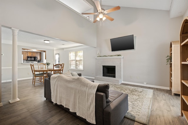living room with ceiling fan, dark wood-style flooring, a brick fireplace, high vaulted ceiling, and baseboards