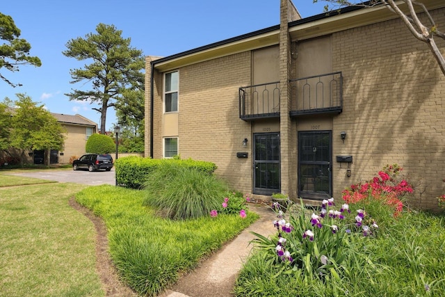 exterior space featuring brick siding, a balcony, and a front yard