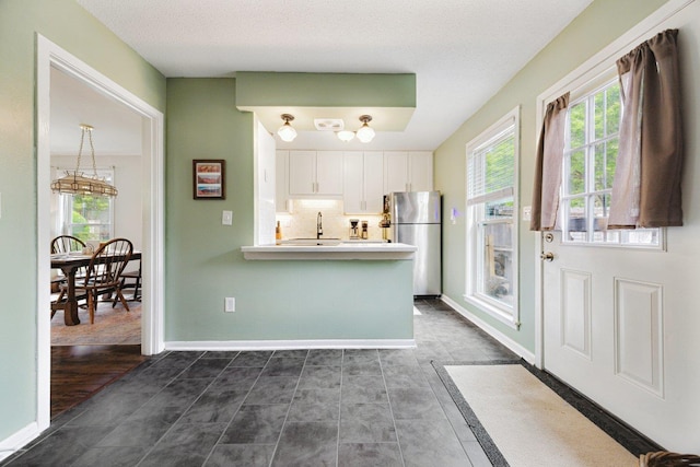 kitchen with a wealth of natural light, freestanding refrigerator, white cabinetry, and a chandelier