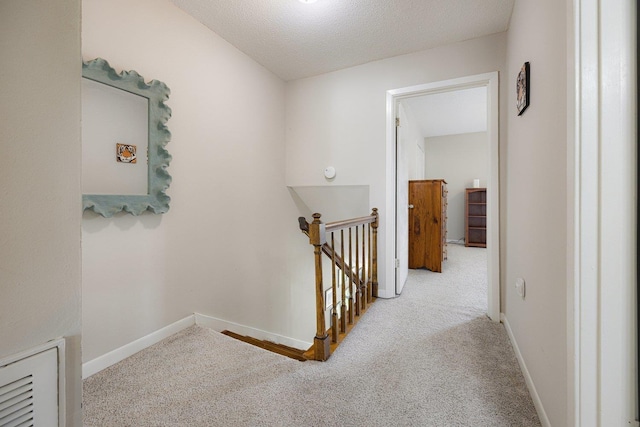corridor featuring baseboards, carpet, a textured ceiling, and an upstairs landing