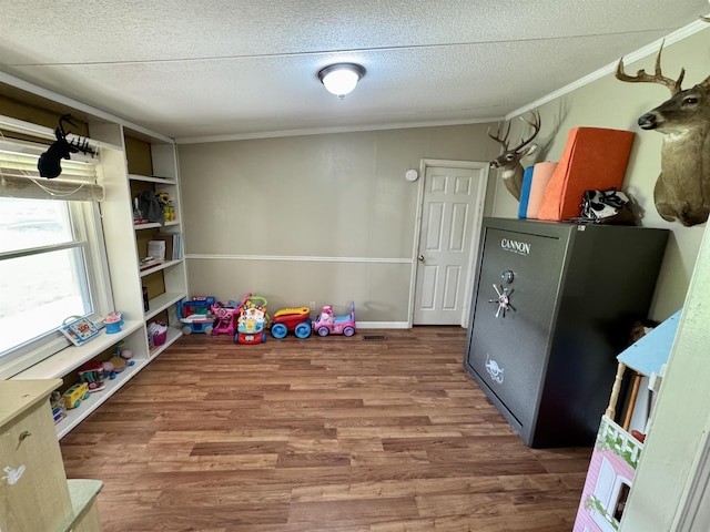 rec room with a textured ceiling, ornamental molding, and wood finished floors