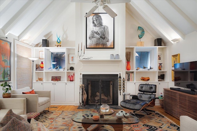 living area with a fireplace with flush hearth, a ceiling fan, beam ceiling, and wood finished floors