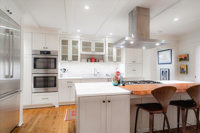kitchen featuring a breakfast bar, a sink, stainless steel appliances, white cabinetry, and island range hood