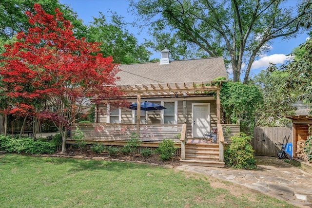 view of front facade with fence, roof with shingles, a pergola, a front lawn, and a wooden deck