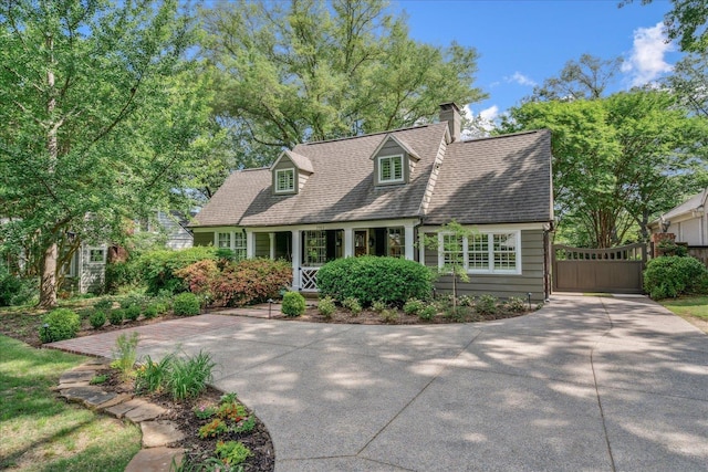 cape cod home with roof with shingles, covered porch, a chimney, and concrete driveway