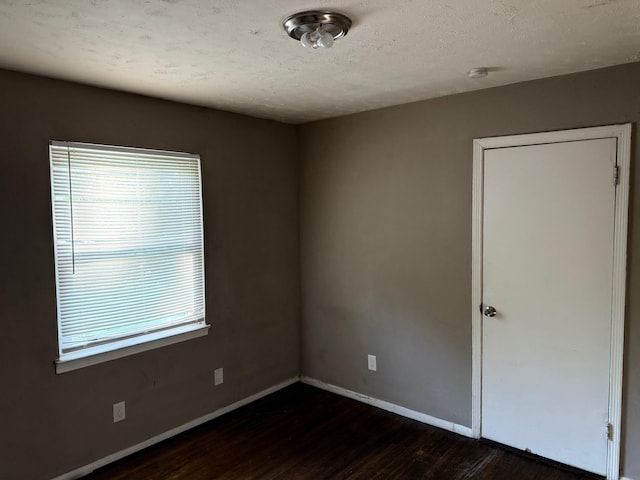 spare room featuring baseboards, a textured ceiling, and dark wood-style floors