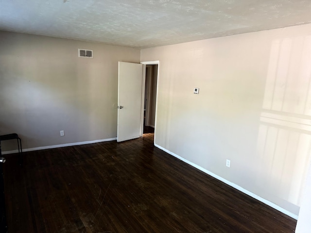 empty room with baseboards, dark wood finished floors, a textured ceiling, and visible vents