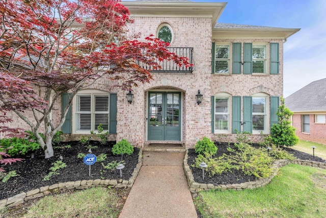 view of front of home with french doors, brick siding, and a balcony