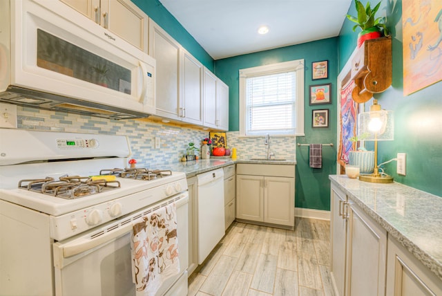 kitchen with light stone countertops, a sink, white appliances, decorative backsplash, and light wood-type flooring