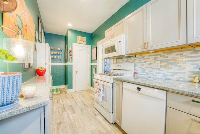 kitchen featuring light stone counters, white appliances, light wood-style flooring, baseboards, and backsplash