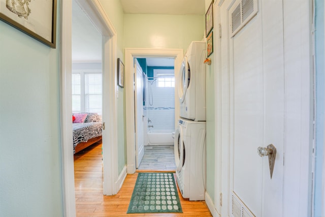 washroom with stacked washing maching and dryer, light wood-style floors, laundry area, and visible vents
