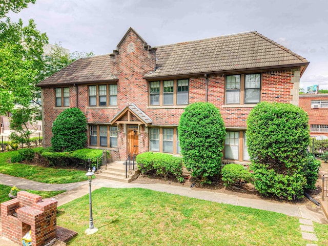 tudor house with brick siding, fence, a tiled roof, and a front yard