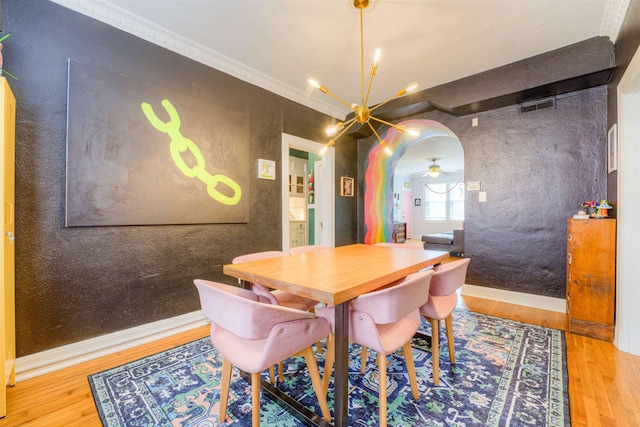 dining room with visible vents, arched walkways, wood finished floors, ceiling fan with notable chandelier, and ornamental molding