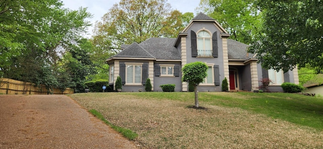 traditional-style home featuring stucco siding, a shingled roof, fence, and a front yard