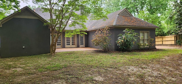 rear view of house featuring fence, roof with shingles, stucco siding, a patio, and a yard
