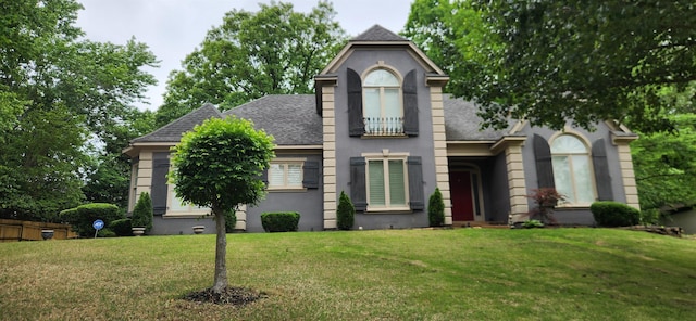 traditional-style house with a shingled roof, a front lawn, and stucco siding
