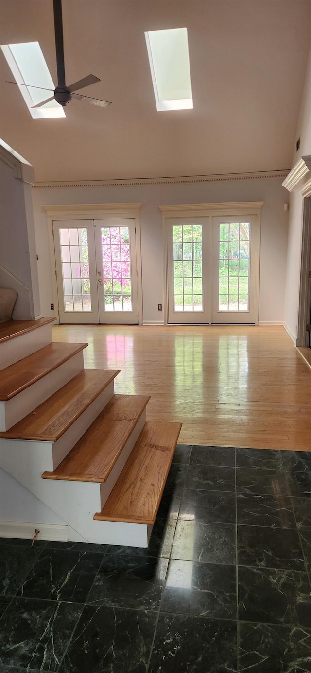 unfurnished living room with stairs, baseboards, ceiling fan, vaulted ceiling with skylight, and french doors