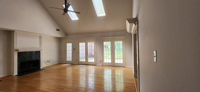 unfurnished living room with a fireplace, high vaulted ceiling, a ceiling fan, light wood-type flooring, and a skylight