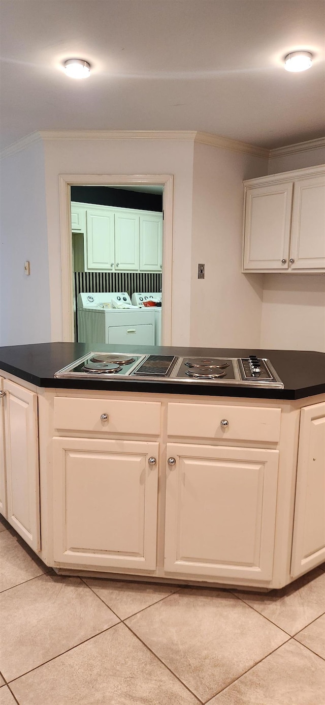 kitchen with crown molding, dark countertops, washer / clothes dryer, white cabinetry, and light tile patterned floors