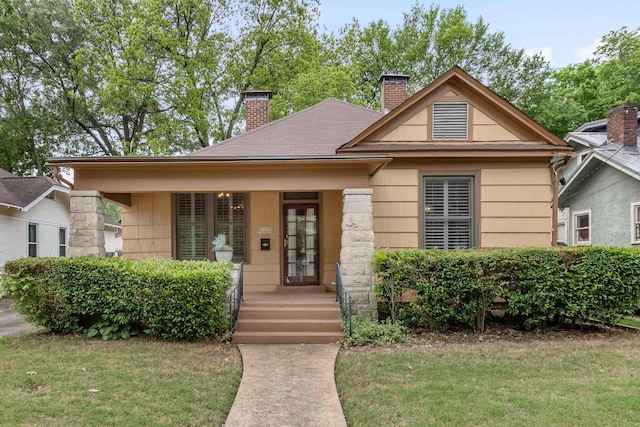 bungalow-style house featuring a porch, a front yard, and a chimney