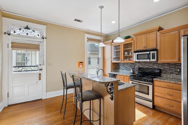 kitchen featuring visible vents, ornamental molding, a center island with sink, appliances with stainless steel finishes, and backsplash