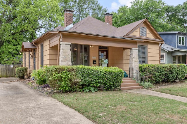 bungalow-style house featuring fence, a shingled roof, a front lawn, stone siding, and a chimney