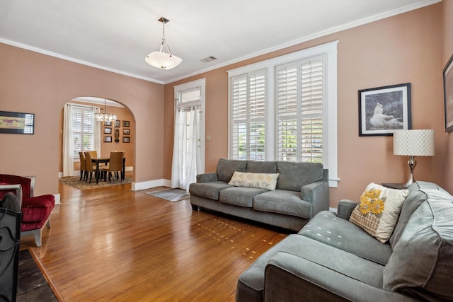 living room featuring visible vents, arched walkways, wood finished floors, an inviting chandelier, and ornamental molding