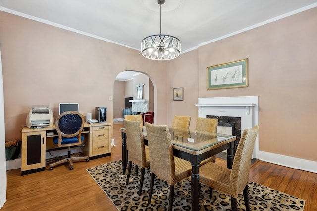 dining room with light wood finished floors, a premium fireplace, arched walkways, baseboards, and ornamental molding