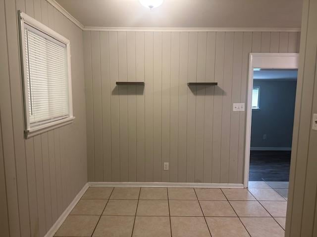 unfurnished room with baseboards, wood walls, and light tile patterned flooring