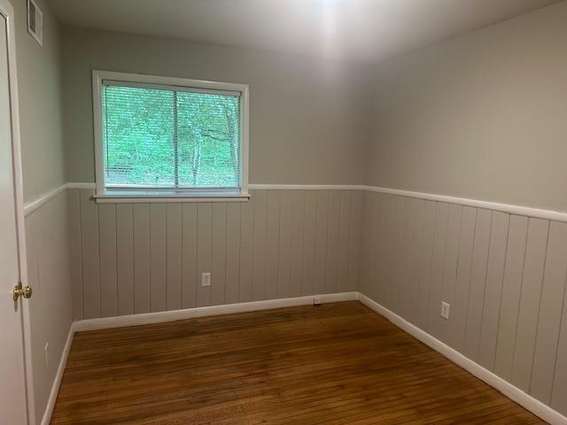 unfurnished room featuring baseboards, visible vents, wood finished floors, and a wainscoted wall