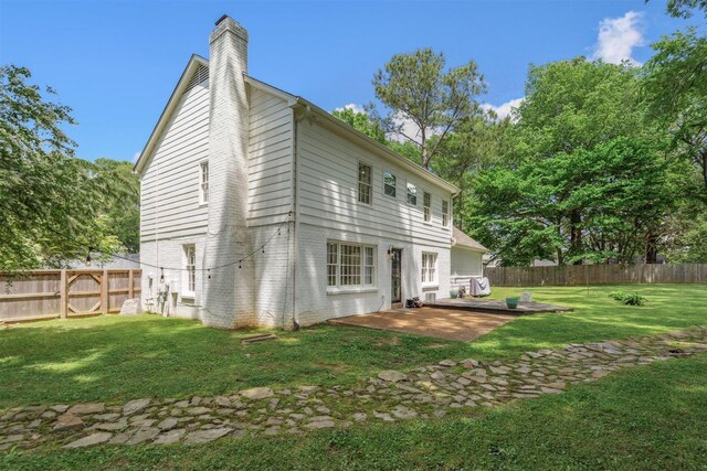 back of property with brick siding, a fenced backyard, a chimney, a lawn, and a patio