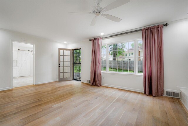 unfurnished room with a ceiling fan, visible vents, a barn door, and light wood-style flooring