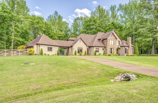 view of front facade with a chimney, fence, a front lawn, a shingled roof, and stone siding