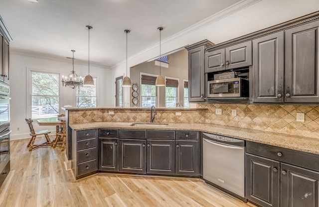 kitchen with a sink, a peninsula, a chandelier, light wood-style floors, and stainless steel appliances