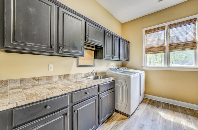 clothes washing area with baseboards, washer and clothes dryer, light wood-style flooring, a sink, and cabinet space