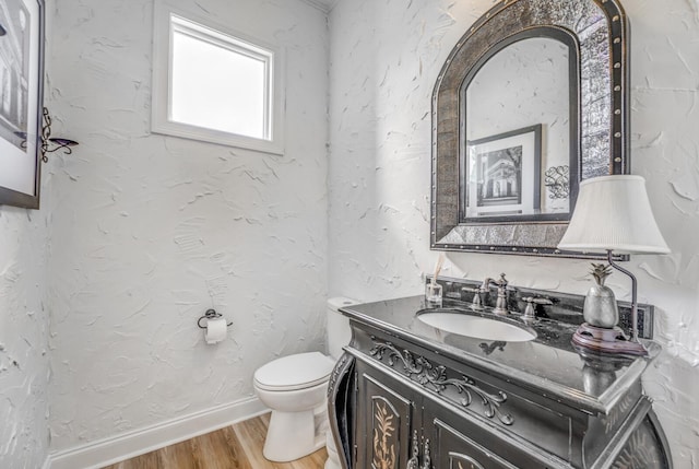 half bathroom with vanity, baseboards, wood finished floors, and toilet