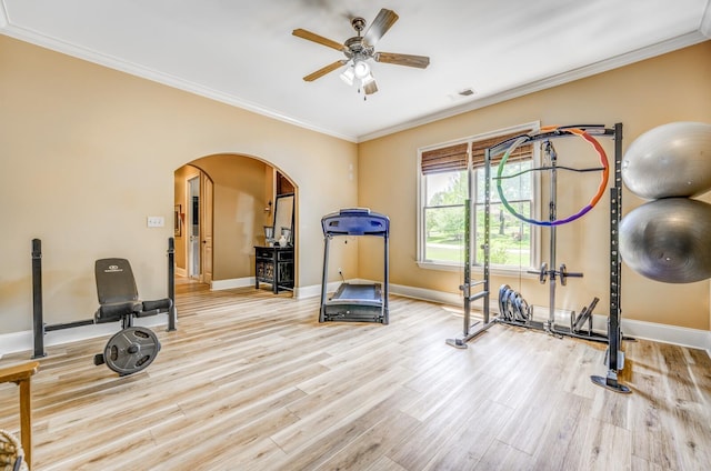 exercise area featuring arched walkways, a ceiling fan, baseboards, wood finished floors, and ornamental molding
