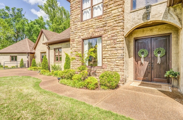 entrance to property featuring a shingled roof, a yard, and stone siding