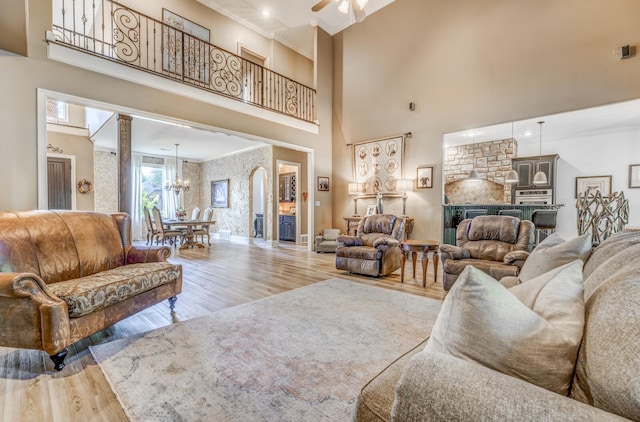 living area featuring wood finished floors, baseboards, ornamental molding, ceiling fan with notable chandelier, and a high ceiling
