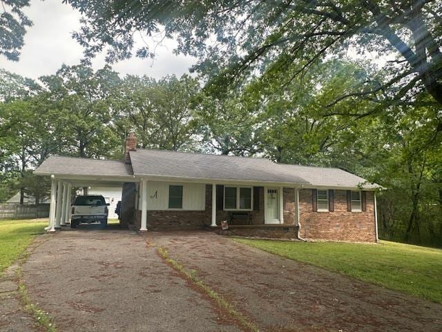 ranch-style home with a front yard, an attached carport, a chimney, brick siding, and driveway