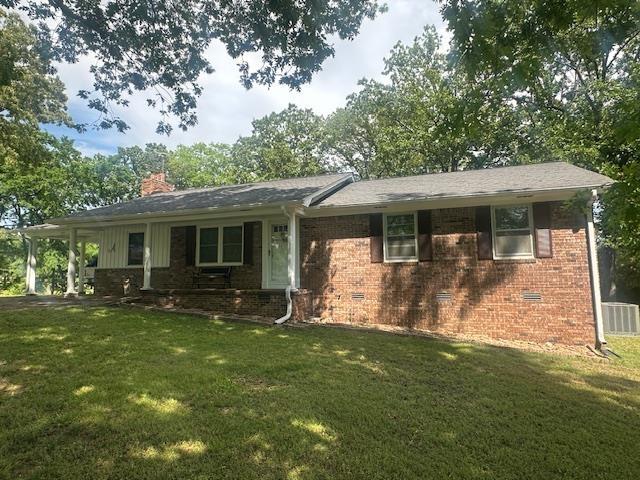 ranch-style home featuring brick siding, cooling unit, a chimney, and a front lawn