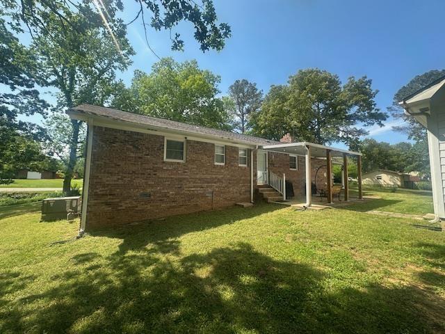 back of house with brick siding, a yard, crawl space, and entry steps