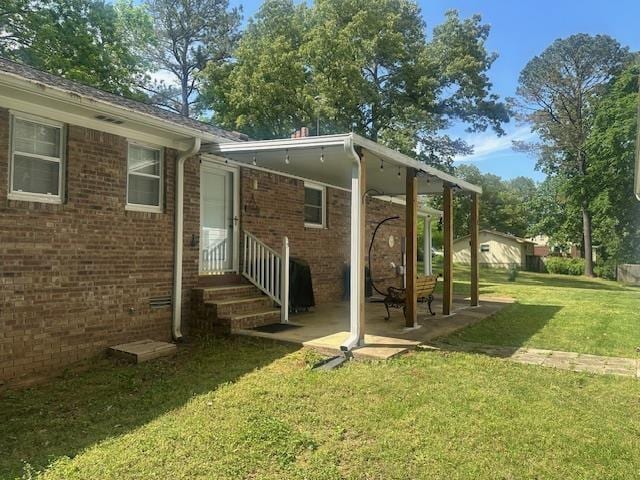 rear view of house featuring a lawn, a patio, entry steps, and brick siding
