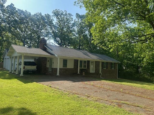 ranch-style home featuring a chimney, an attached carport, driveway, and a front yard