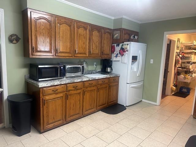 kitchen featuring crown molding, white fridge with ice dispenser, stainless steel microwave, and brown cabinets