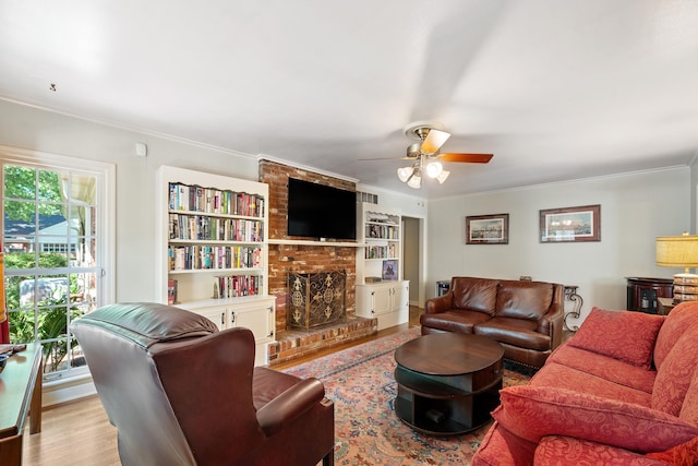 living area featuring ornamental molding, a fireplace, a ceiling fan, and built in shelves